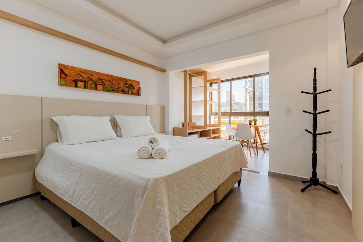 Une chambre d’hôtel avec un grand lit, un tableau au mur, un porte-manteau et une vue sur l’extérieur.