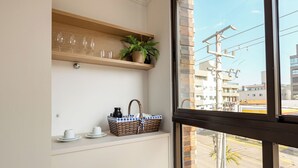 A corner of a room with a shelf holding wine glasses, a potted plant, and a wicker basket with cups. - Kia Ora Suítes (Bombinhas)