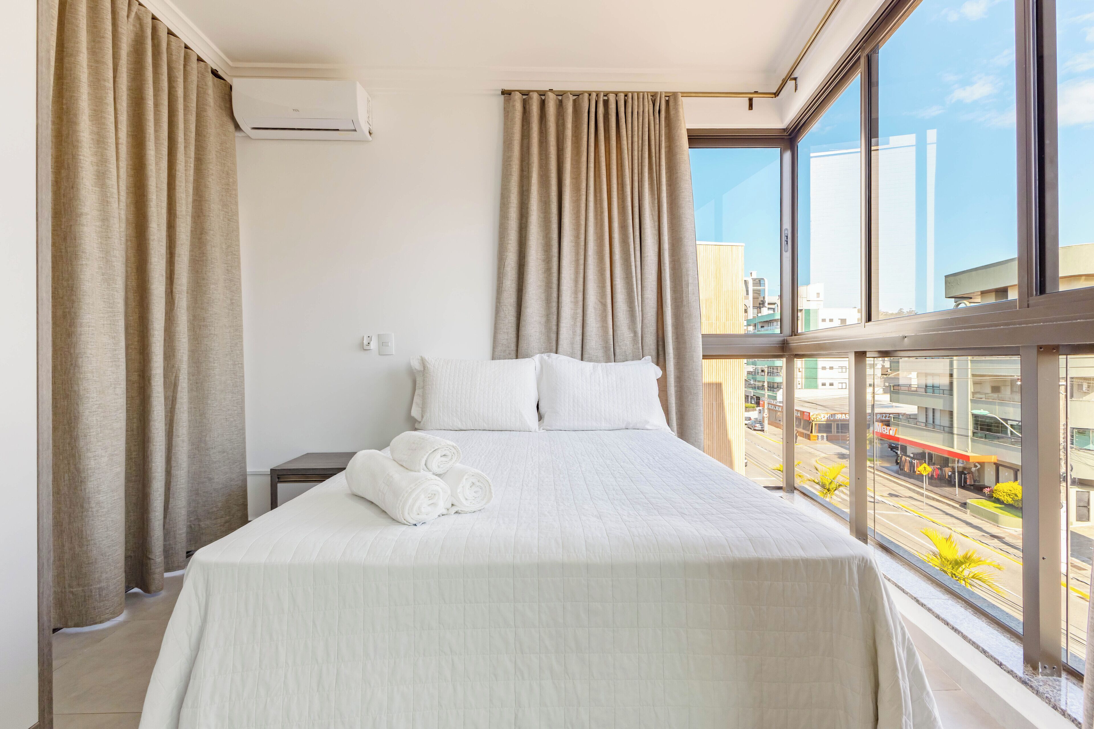 Habitación de hotel con una cama grande, cortinas color beige y vistas a la ciudad a través de la ventana.