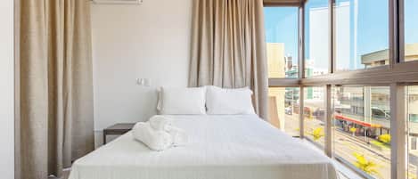Habitación de hotel con una cama grande, cortinas color beige y vistas a la ciudad a través de la ventana.