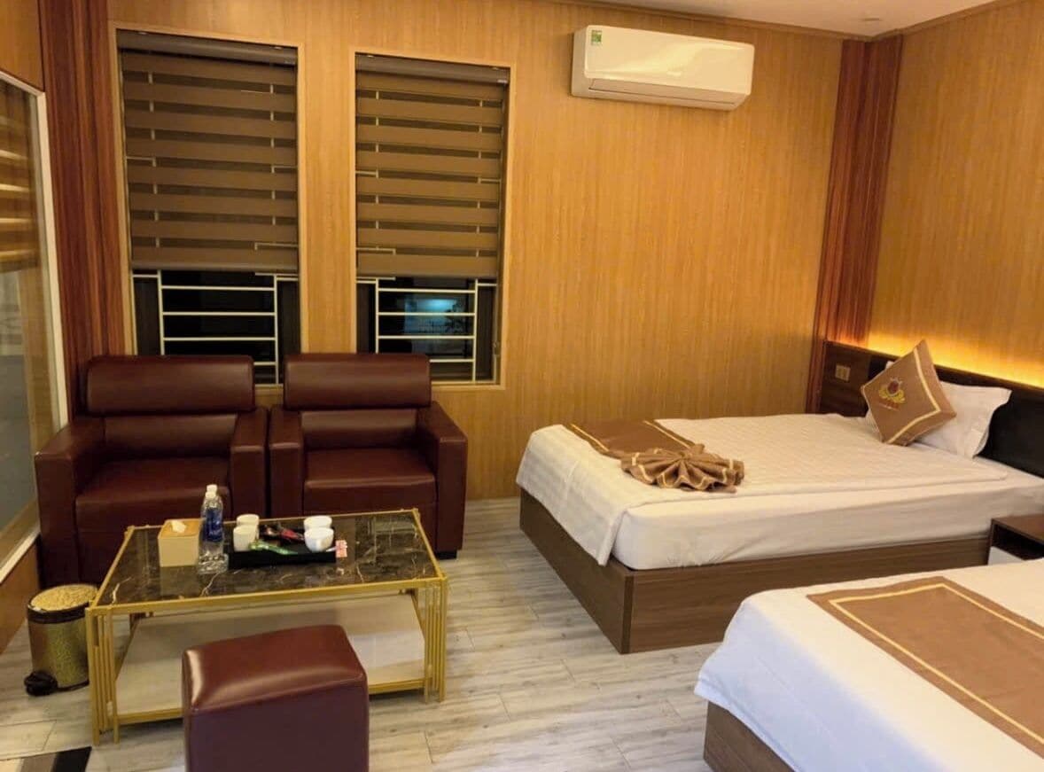 A hotel room with a bed, two brown leather chairs, a glass coffee table, and a small trash bin.