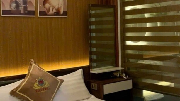 Habitación de hotel con cama, mesita de noche, espejo y ventana con persianas.