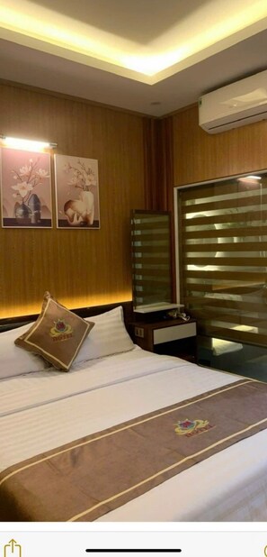 A hotel room with a bed, a nightstand, a mirror, and a window with blinds. - 3M Hotel PT - by BAY LUXURY (Phu Tho)