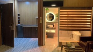 Un espacio habitable compacto con kitchenette, un baño con inodoro y lavabo, y un televisor sobre el lavabo.