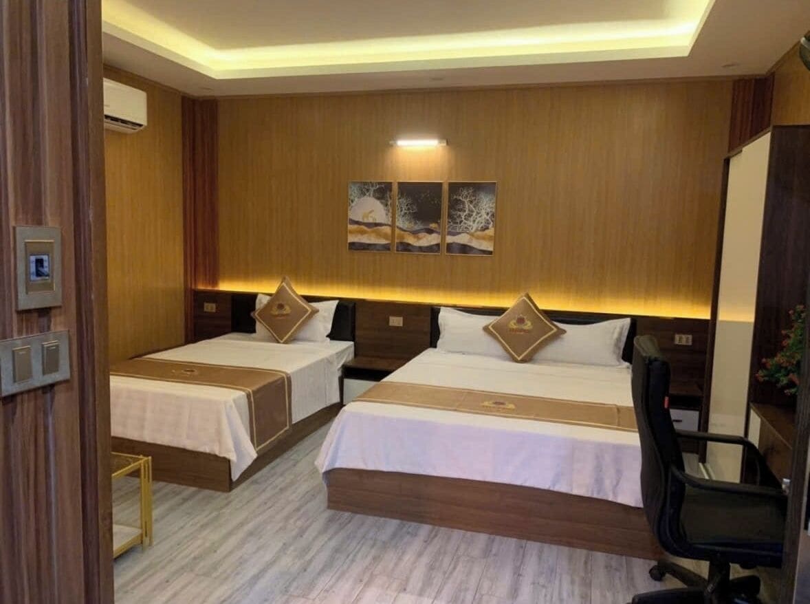 A hotel room with two beds, a desk, and a chair. There are wall-mounted air conditioning units and a ceiling light.