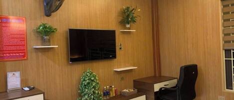 Une chambre d’hôtel avec un mur recouvert de panneaux de bois, un téléviseur à écran plat fixé au-dessus d’un bureau, un fauteuil de bureau noir, une petite plante en pot et un bureau avec des tiroirs.