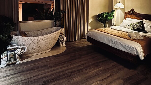 Habitación de hotel con techo de madera, una bañera grande, cama con cabecera de madera y ventana con cortinas.