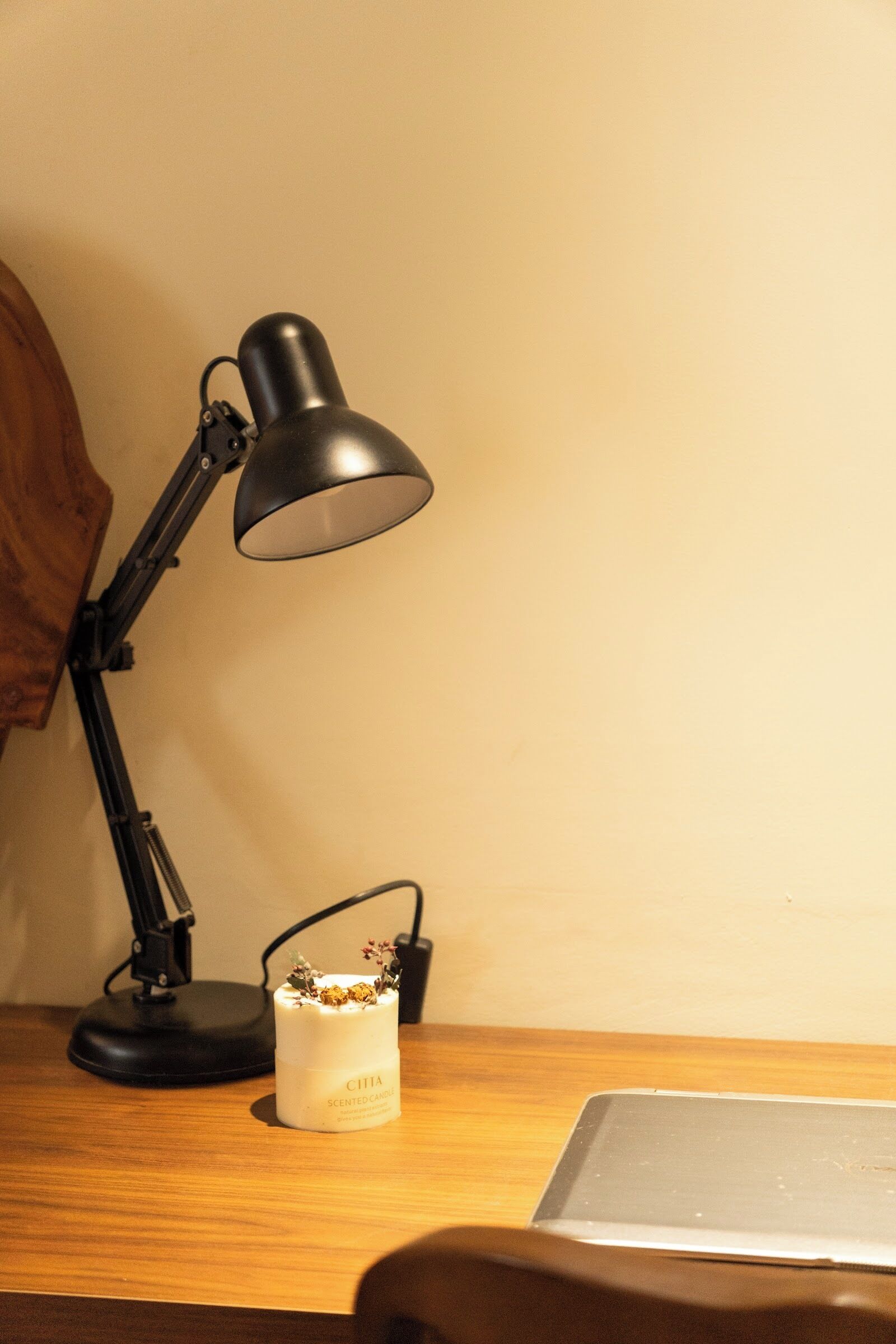 A desk with a black desk lamp, a white scented candle, and a laptop.