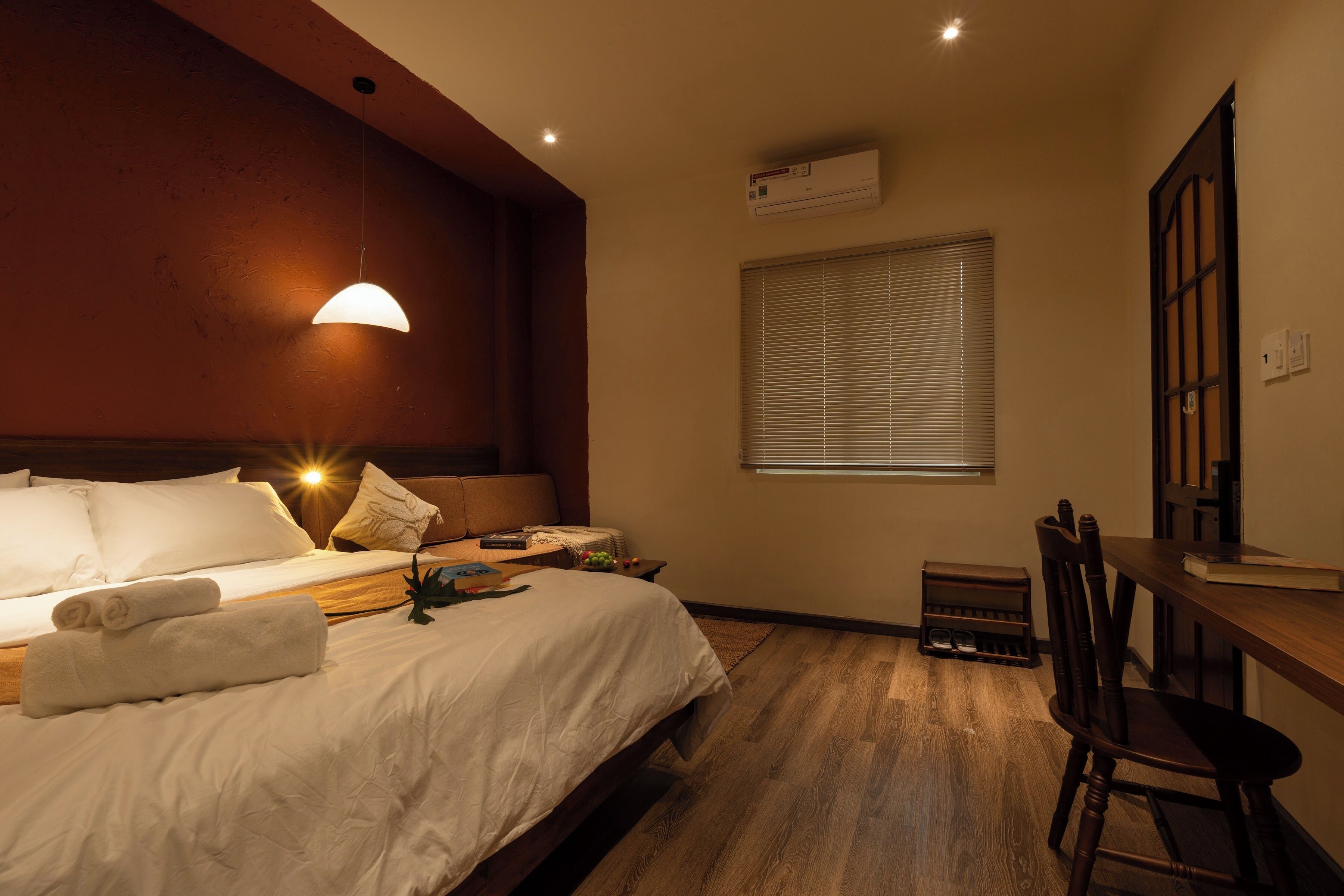 Habitación de hotel con cama, escritorio, silla, ventana con persianas y unidad de aire acondicionado.