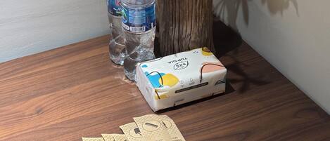 A wooden table with a potted plant, water bottles, a box of tissues, and a pair of earplugs.