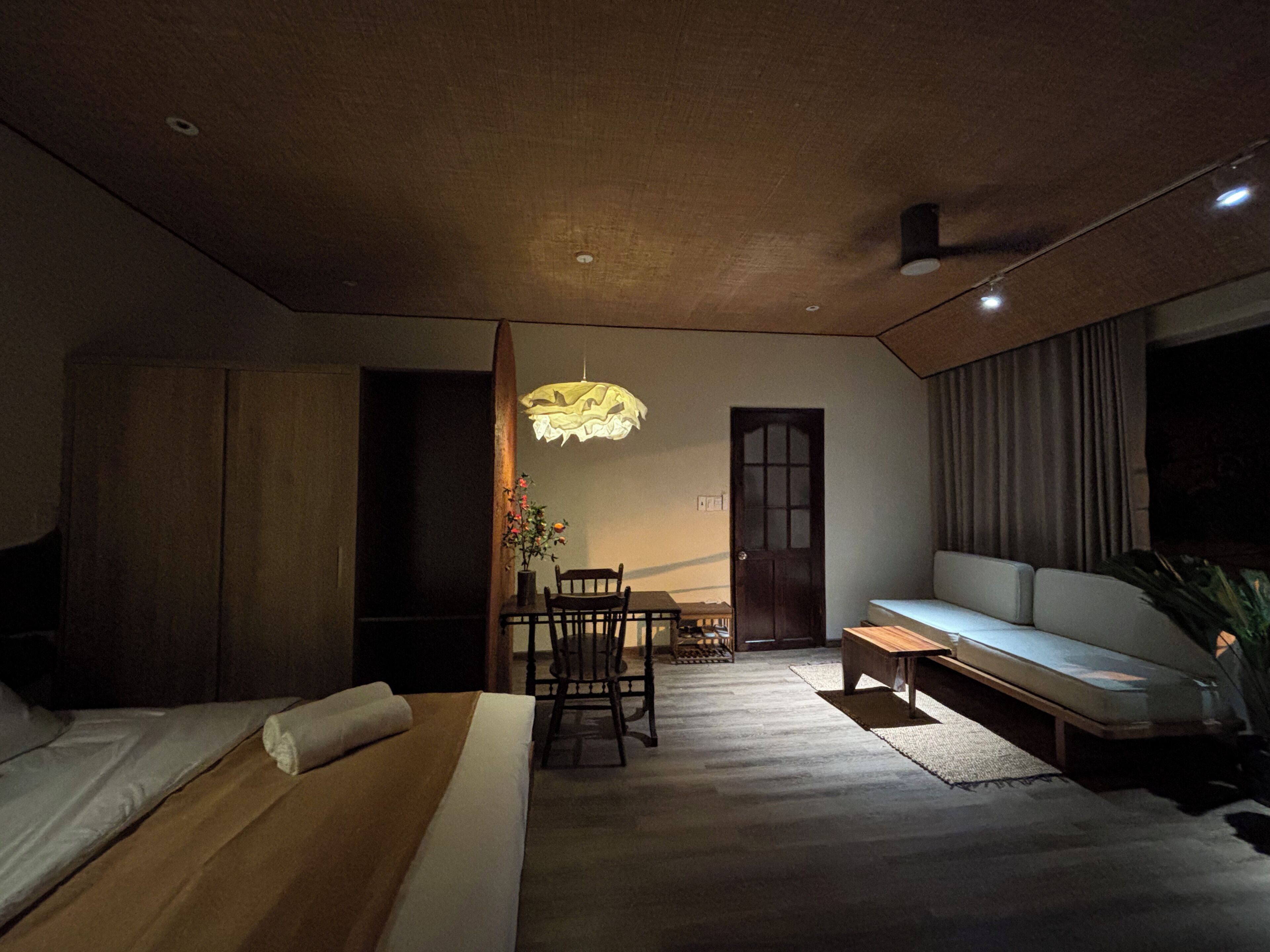 A modern bedroom with a bed, a bench, a dining table with chairs, and a hanging light fixture.