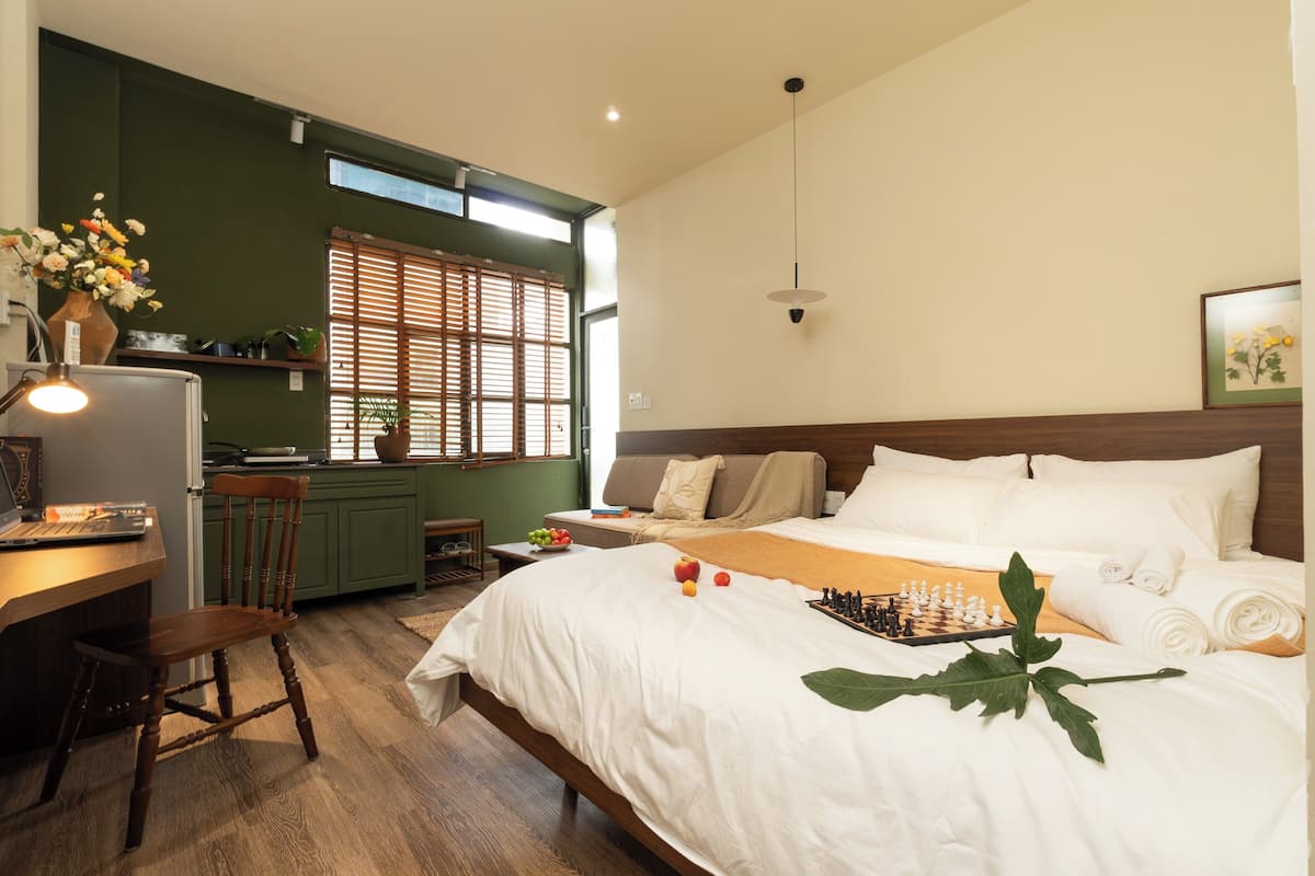 Un dormitorio con cama, escritorio, silla, ventana con persianas, lámpara colgante y un tablero de ajedrez.