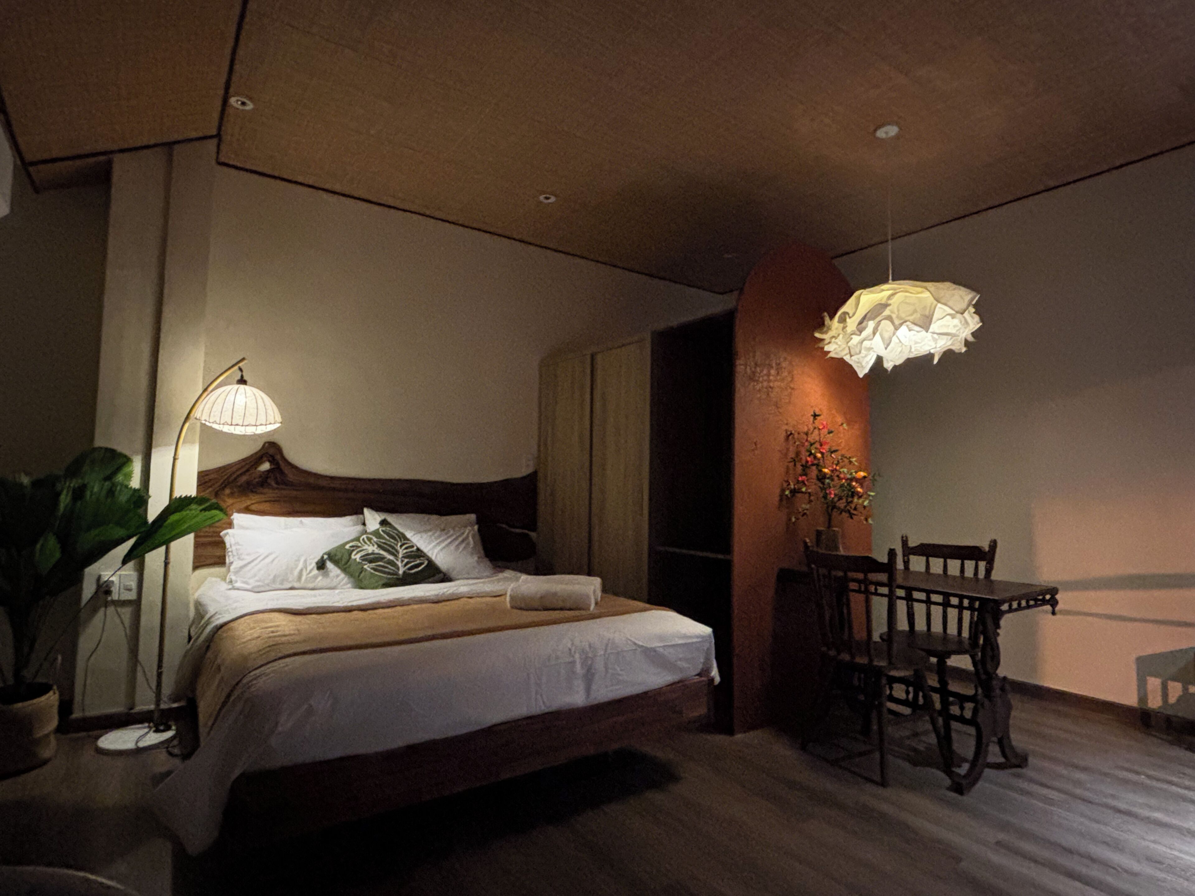 A bedroom with a bed, bedside table, lamp, and a dining area with chairs and a table.