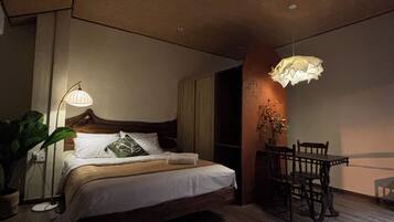 A bedroom with a bed, bedside table, lamp, and a dining area with chairs and a table.