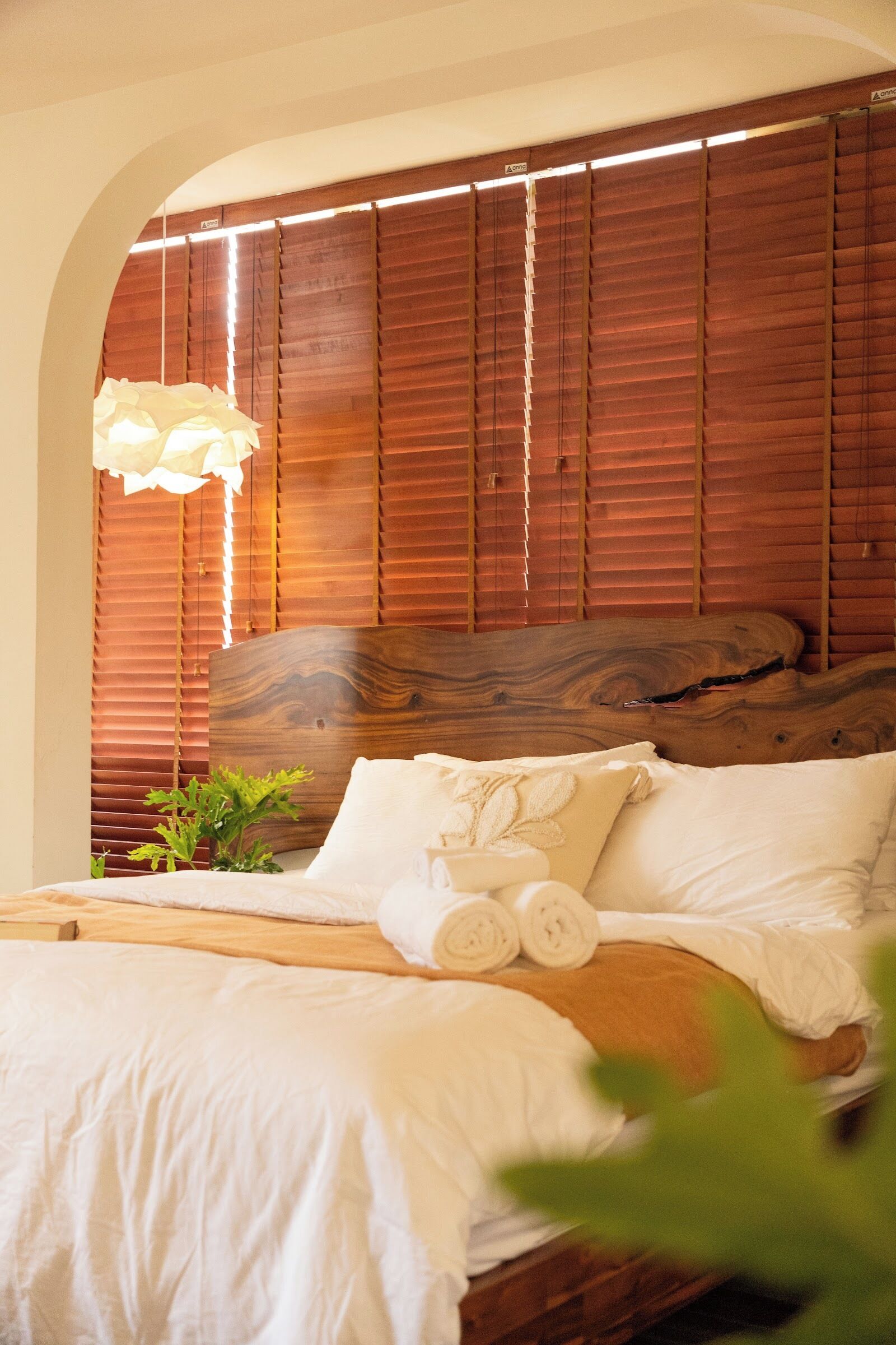 A bedroom with a wooden headboard, a bed with white linens, a hanging light fixture, and a small plant.