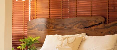 A bedroom with a wooden headboard, a bed with white linens, a hanging light fixture, and a small plant.