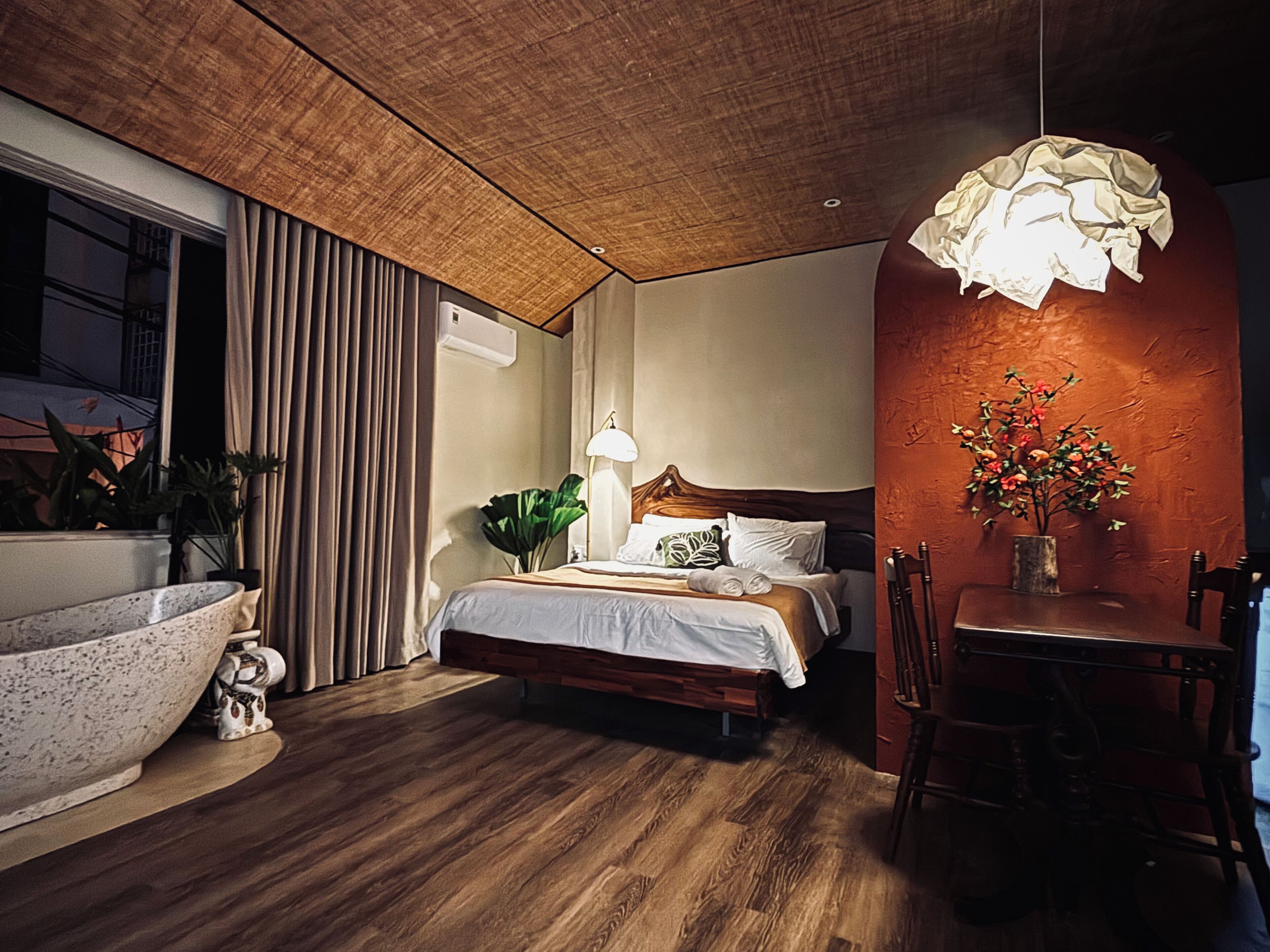 Ein modernes Hotelzimmer mit Holzboden, einem großen Bett mit weißen Leinentüchern, einem Esstisch mit Stühlen und einer Wandvase mit Blumen.