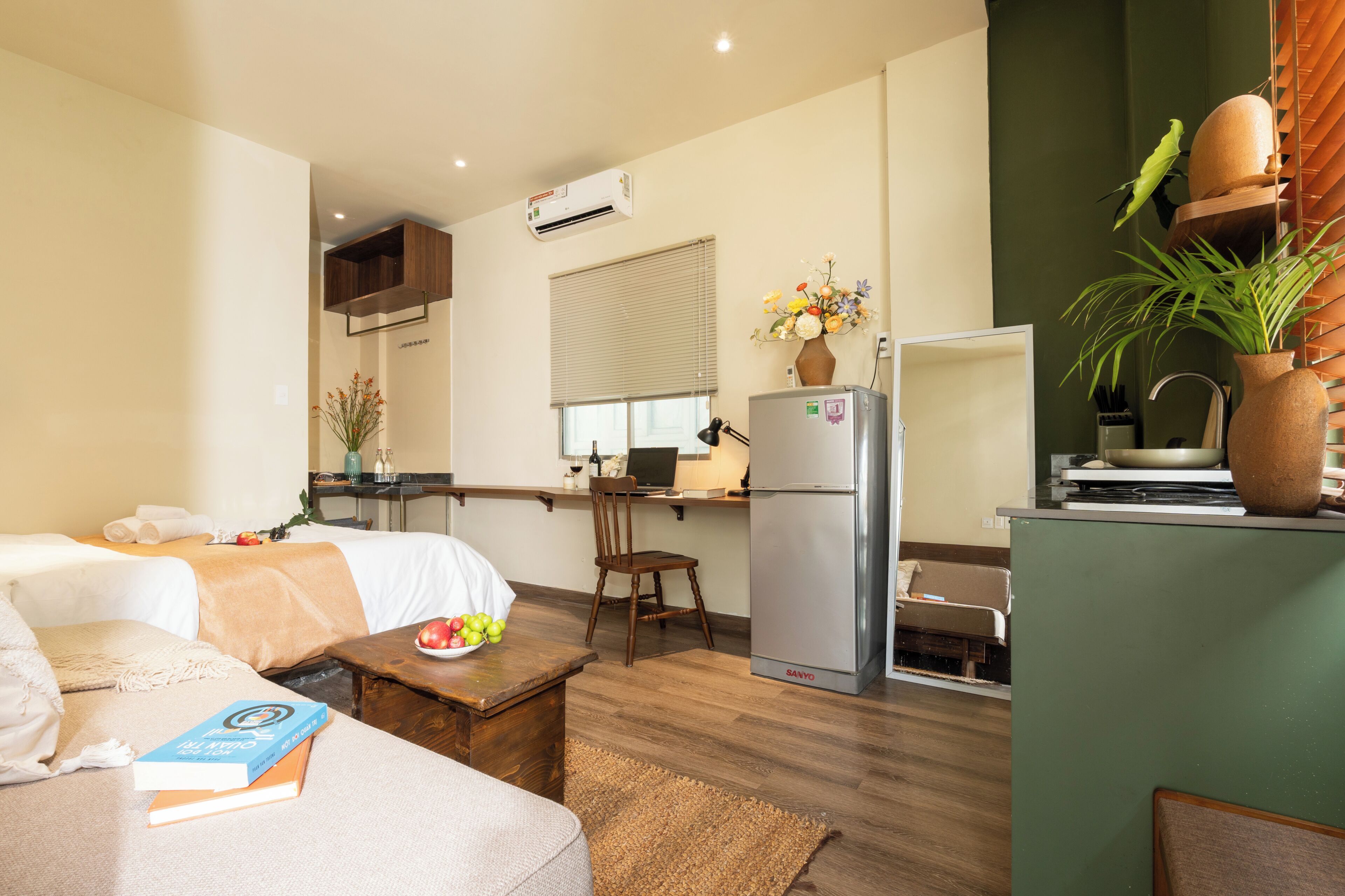 A compact hotel room with a bed, a small desk, a kitchenette, and a dining area.
