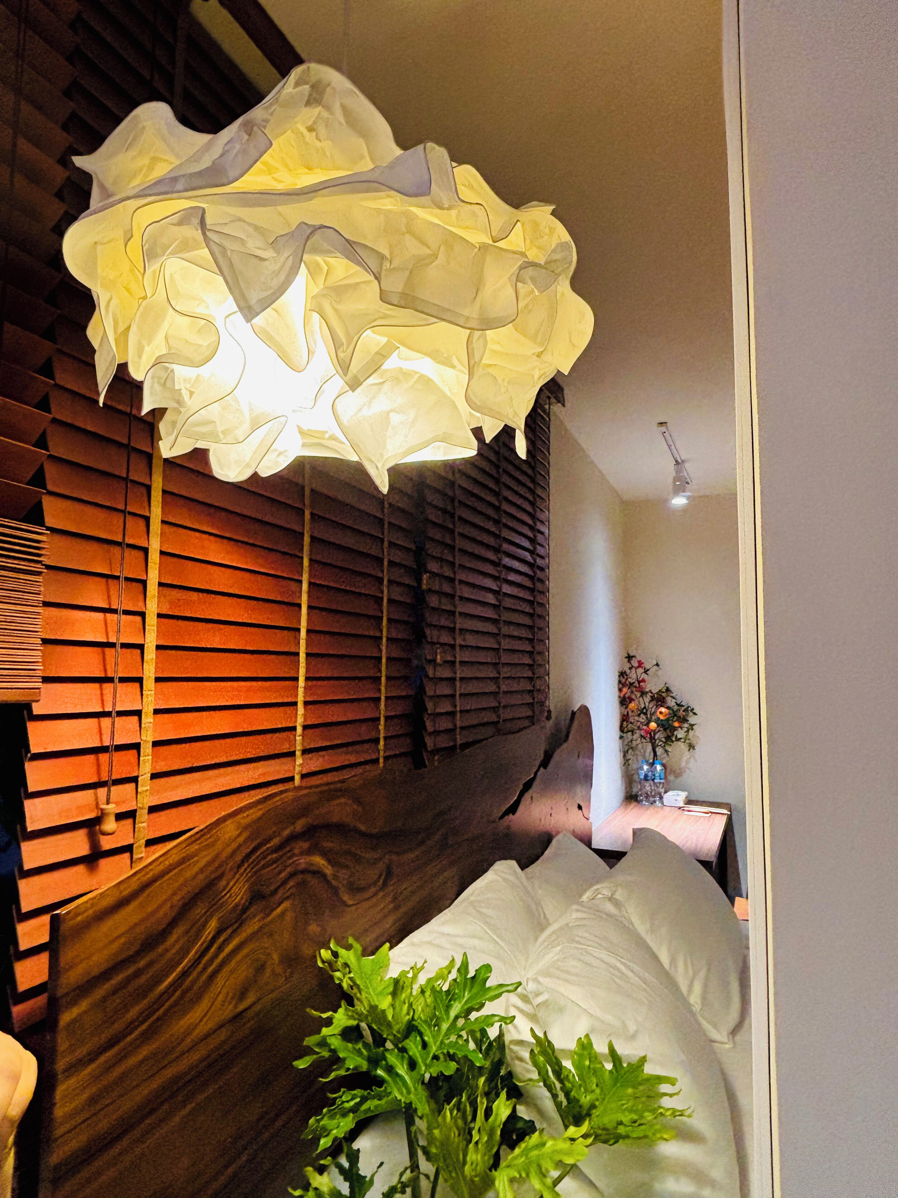 Ein Zimmer mit einer Wand aus Holzlatten, einem Bett mit weißer Bettwäsche, einer Hängeleuchte und einem kleinen Tisch mit einer Vase.