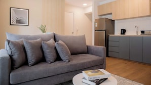 A modern living room with a grey sofa, a coffee table with a book, and a kitchen area with wooden cabinets and appliances. - w Charming 2BR Stay in Miraflores (Lima)