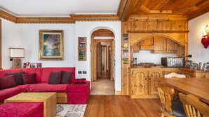A cozy living room with a red sofa, wooden dining table, and kitchen with wooden cabinets.