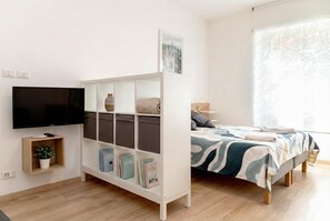 A modern bedroom with a bed, a TV, a bookshelf, and a window with a leaf pattern.