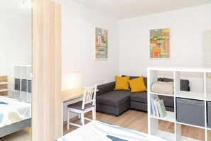 Une pièce moderne avec un canapé gris, une chaise blanche, un bureau avec une lampe et une bibliothèque.