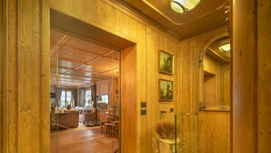 A wooden interior with a glass door leading to a living area with a sofa, dining table, and a large mirror.