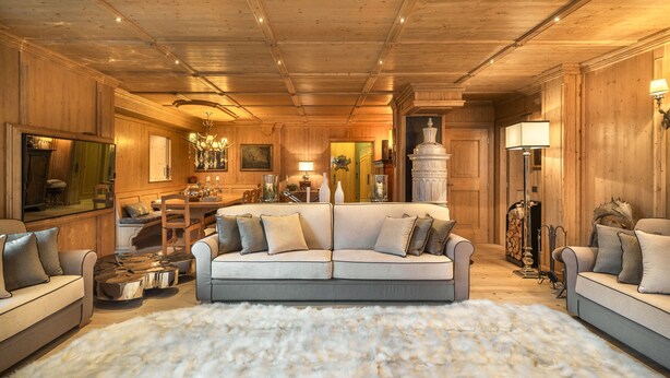 A cozy living room with a large sofa, a coffee table, and a fluffy rug. There is a dining area with a table and chairs, and a fireplace with a decorative vase.