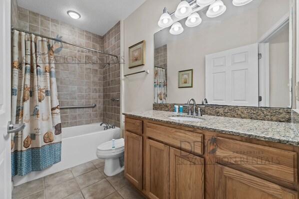 A bathroom with a bathtub, toilet, vanity with sink, wooden cabinets, and a shower curtain with sea creature prints.