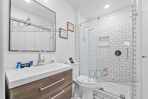 Un baño moderno con tocador blanco, un espejo, inodoro y zona de ducha con mampara de vidrio.