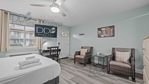 Ein Hotelzimmer mit einem Bett, einem Schreibtisch, zwei Stühlen, einem Deckenventilator und einem Fenster mit Vorhängen.
