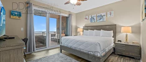 Ein Schlafzimmer mit Bett, Nachttischen, Deckenventilator und einer Schiebeglastür, die auf einen Balkon führt.