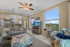 A spacious living room with a ceiling fan, a television, and a large window offering a view of the landscape.