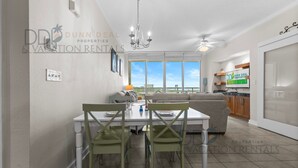 Een moderne keuken met een ingebouwde oven, een eethoek met een witte tafel en groene stoelen, en een groot raam met uitzicht op de stad.
