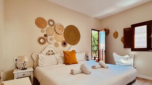 A spacious bedroom with a large bed, a bedside table with a lamp, and decorative woven wall art.
