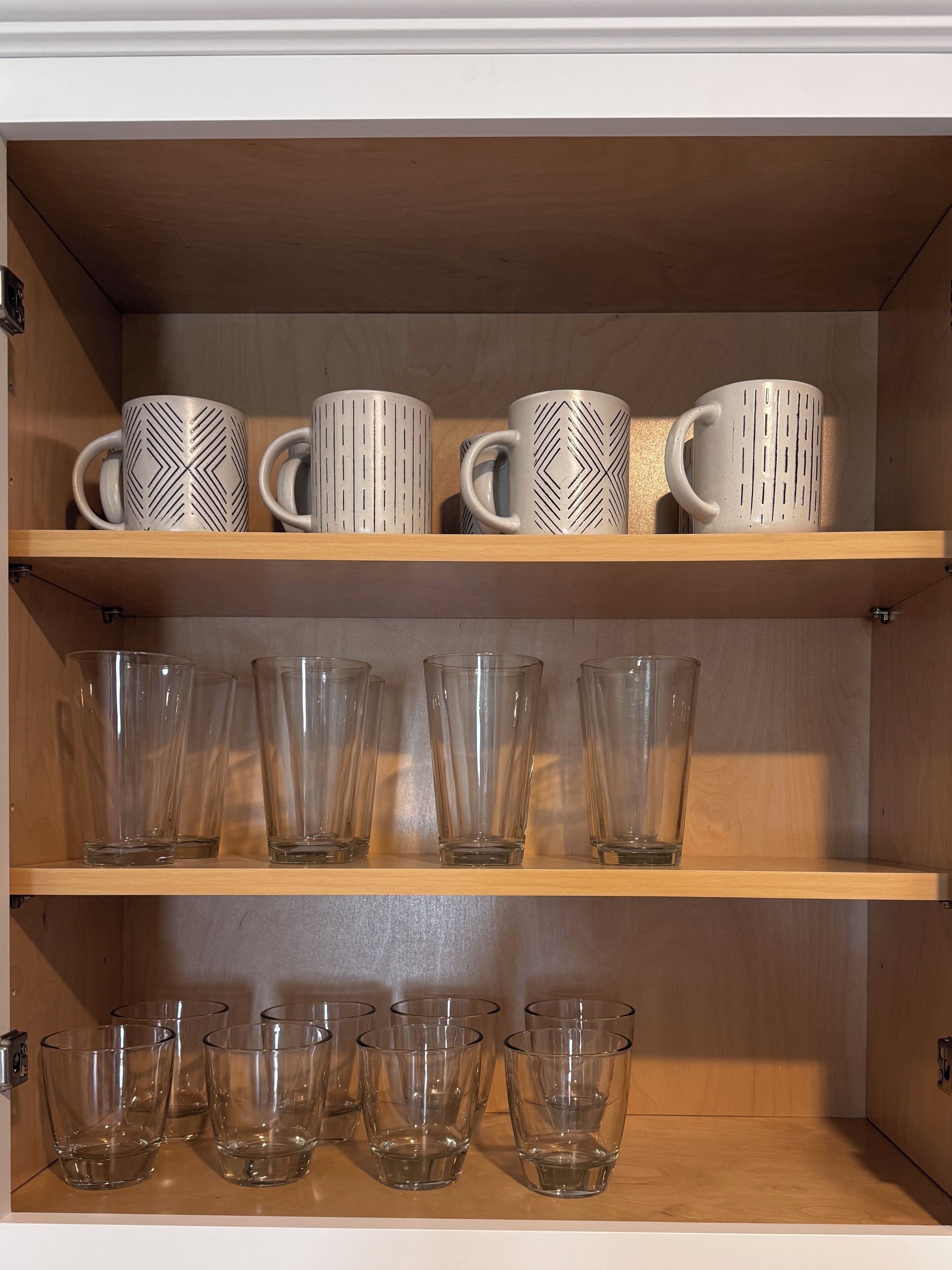 A wooden shelf unit with decorative mugs and clear glass tumblers.