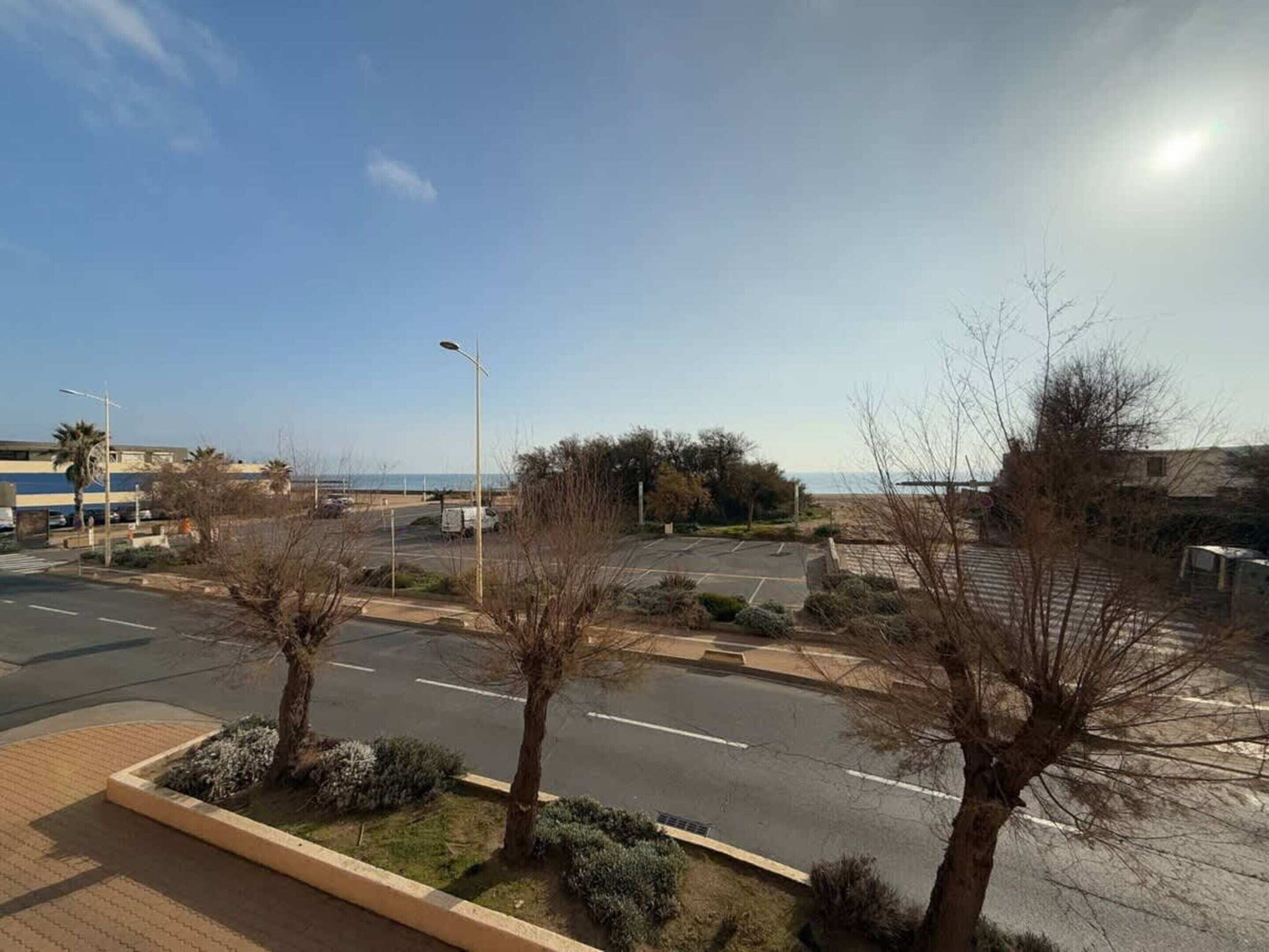 A parking lot with trees and a clear view of the sea.