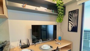 A modern dining area with a TV, two black chairs, a wooden table, and a plant on the wall. - Uwin Brooklin NR (São Paulo)