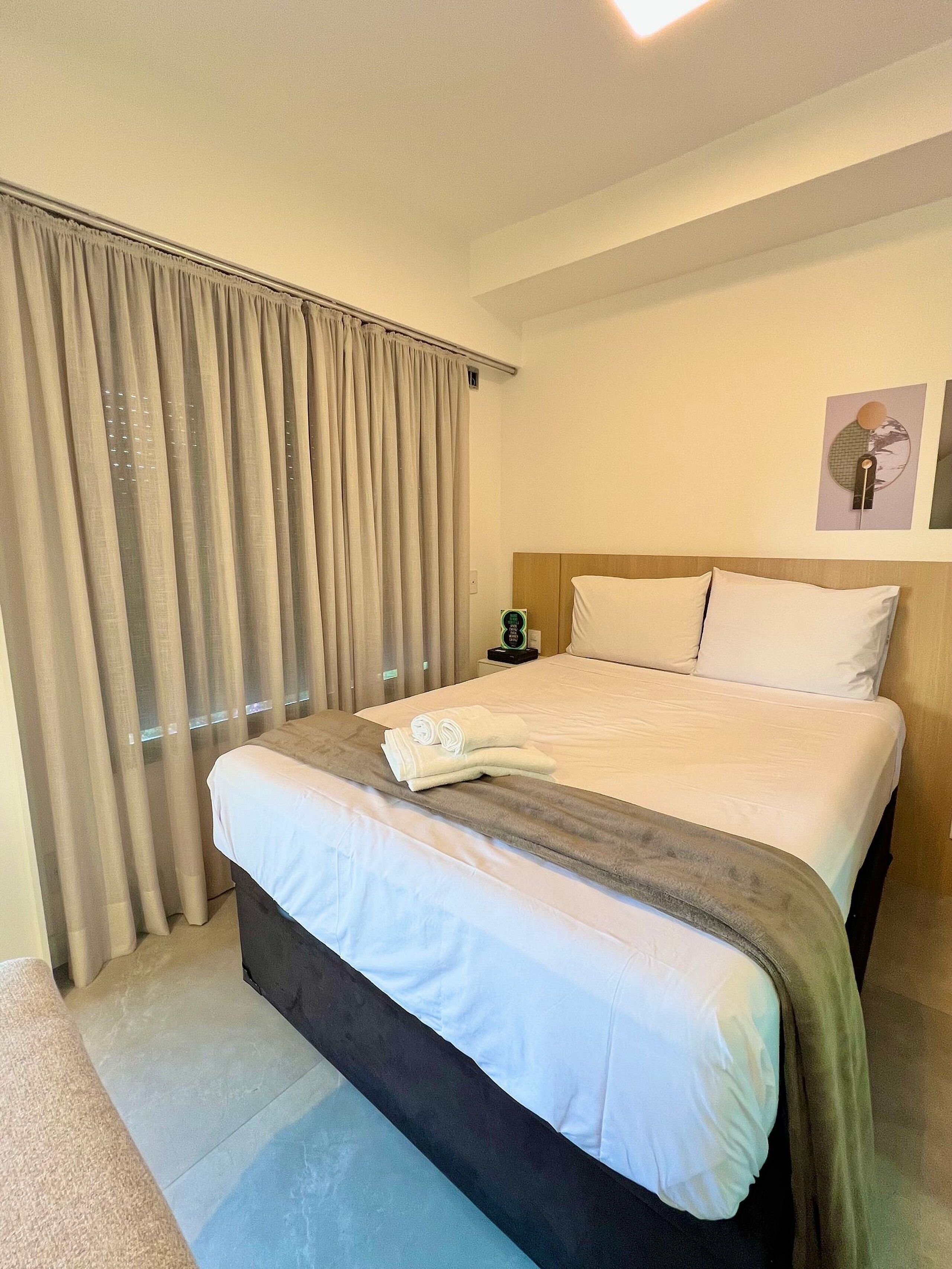 A hotel room with a large bed, a bedside table with a lamp, and a window with curtains.