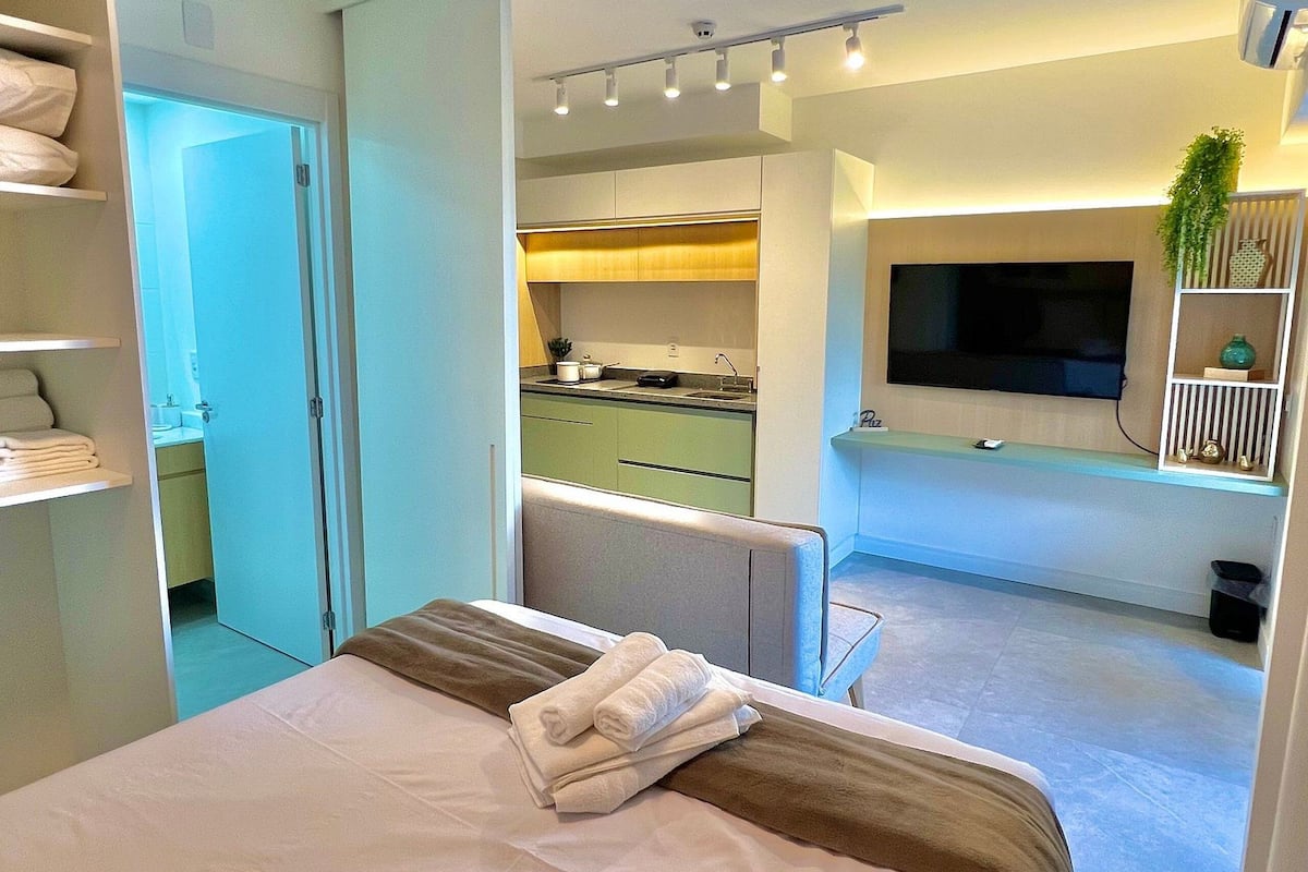 A modern hotel room with a large bed, a TV, and a kitchenette.
