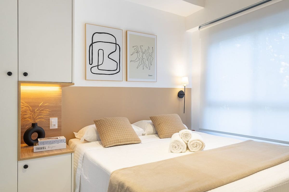 A modern bedroom with a large bed, a bedside table with a lamp, and artwork on the wall.