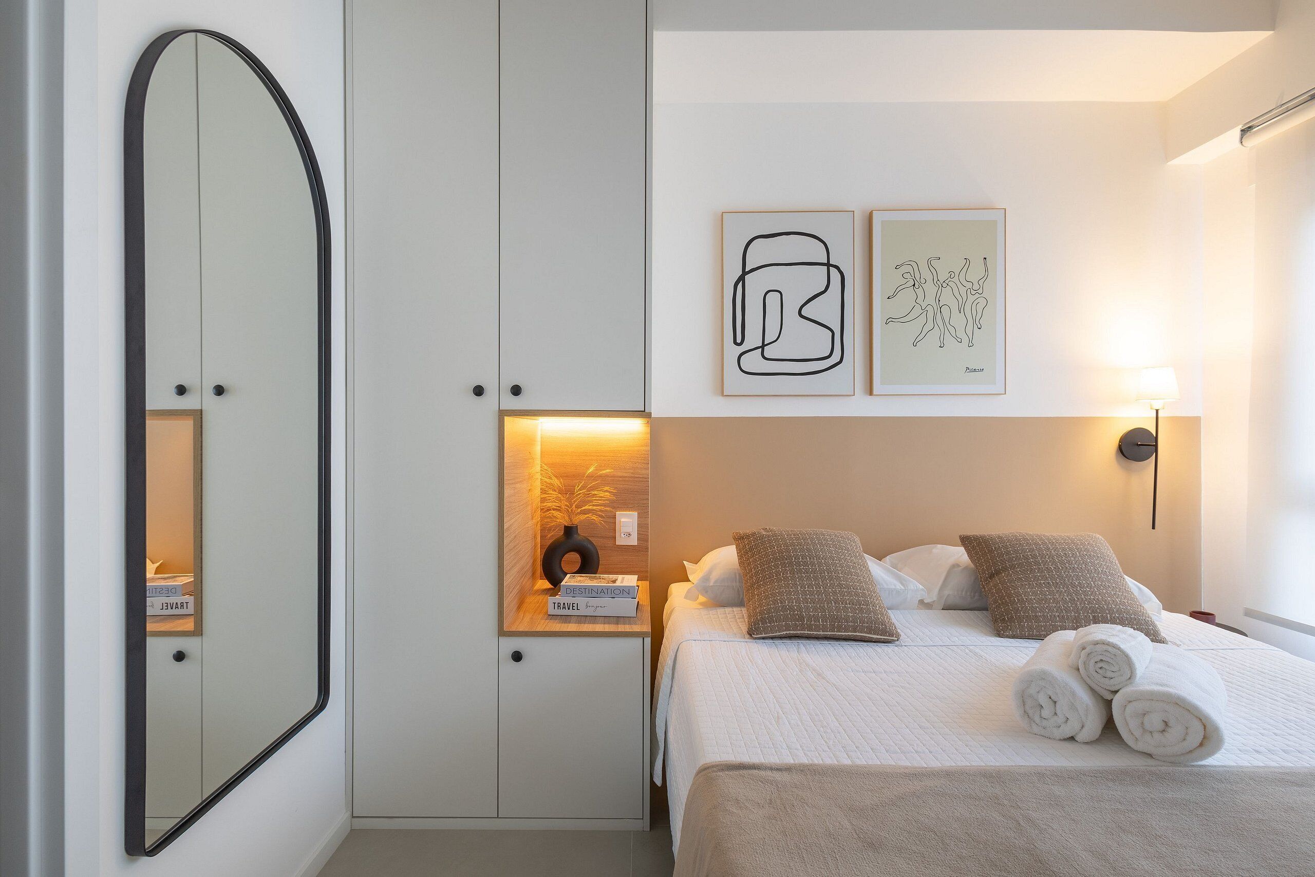 A hotel room with a bed, a nightstand, a mirror, and artwork on the wall.