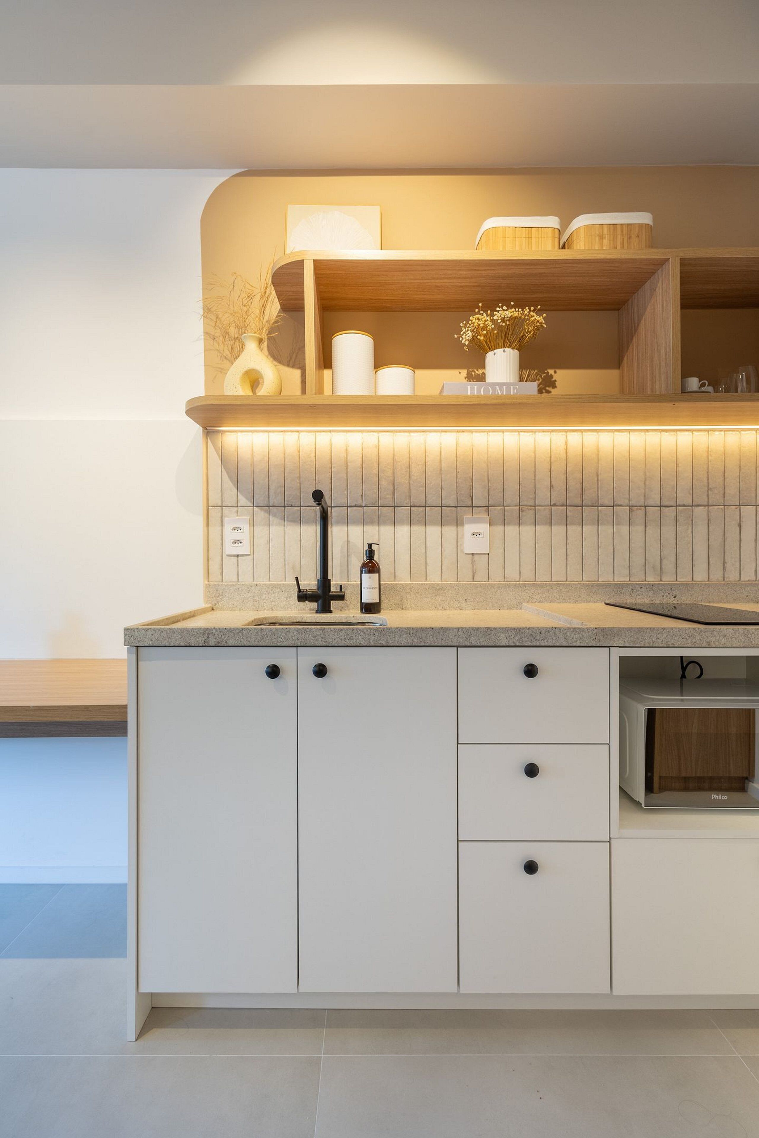Une cuisine moderne dotée d’un évier encastré, de meubles blancs et d’un plan de travail sur lequel se trouvent une bouteille et un vase.