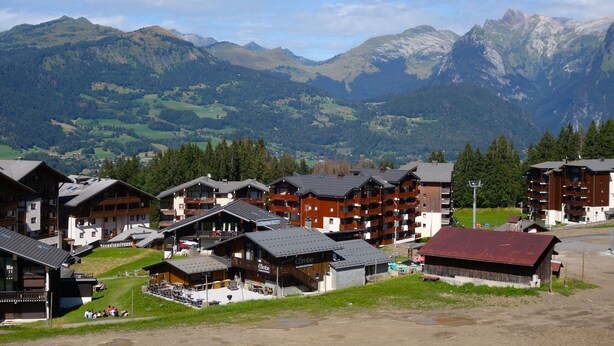 A mountain resort with chalet-style buildings, ski lifts, and a view of the surrounding mountains.