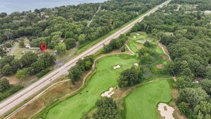 Une vue aérienne d’un terrain de golf comportant plusieurs trous, une route qui longe le terrain et une étendue d’eau en arrière-plan.
