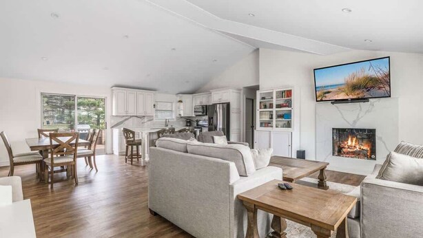 Un vaste espace de vie doté d’une cheminée, un coin repas avec des meubles en bois et une cuisine avec des placards blancs.