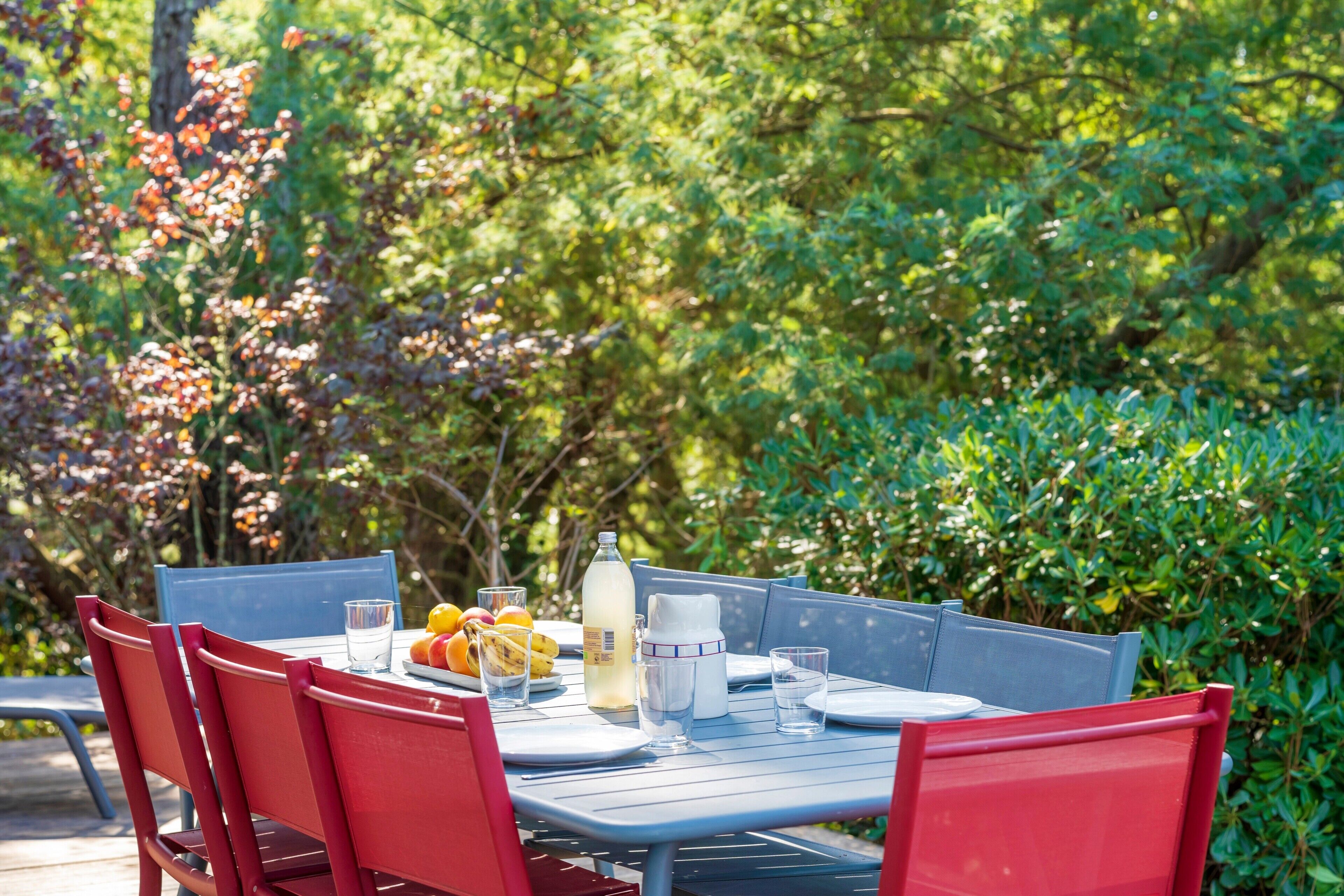 Una mesa de comedor al aire libre con sillas, una botella, vasos y fruta.