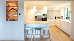 Una cocina moderna con una isla central, taburetes de bar, electrodomésticos de acero inoxidable y un ventanal que proporciona luz natural.