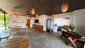 Una habitación amplia con suelo de concreto, muebles de madera, techo estampado y un refrigerador.